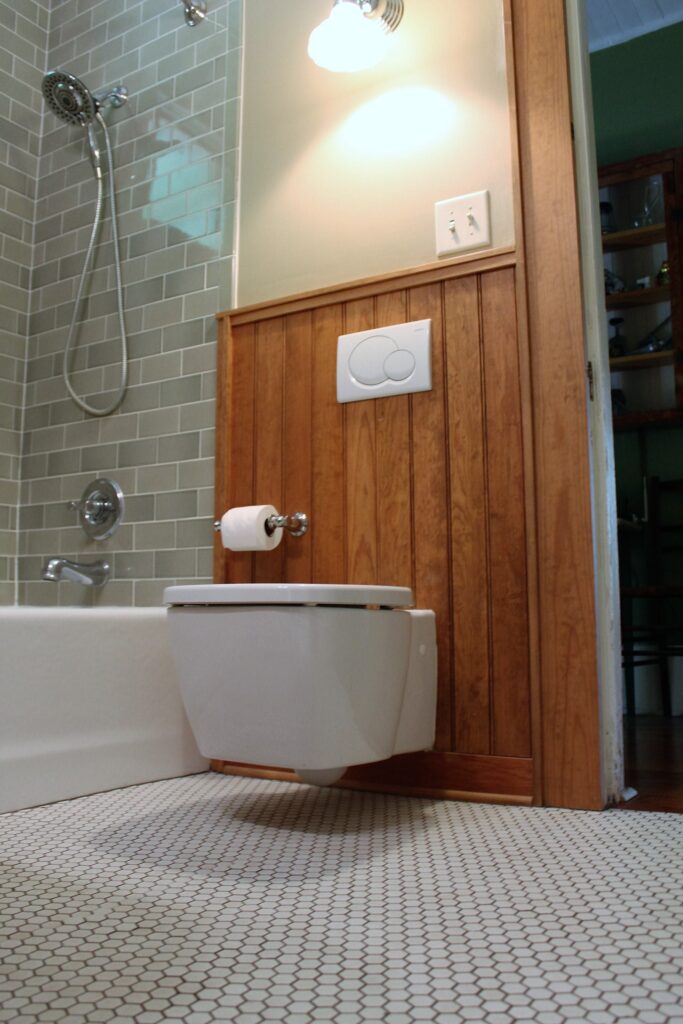 Modern bathroom remodel with wall-mounted toilet and wood accent wall.